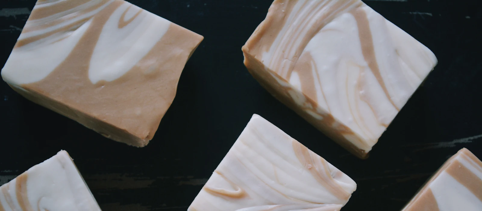 Freshly cut bars of cream and caramel swirled soap on a dark wooden board