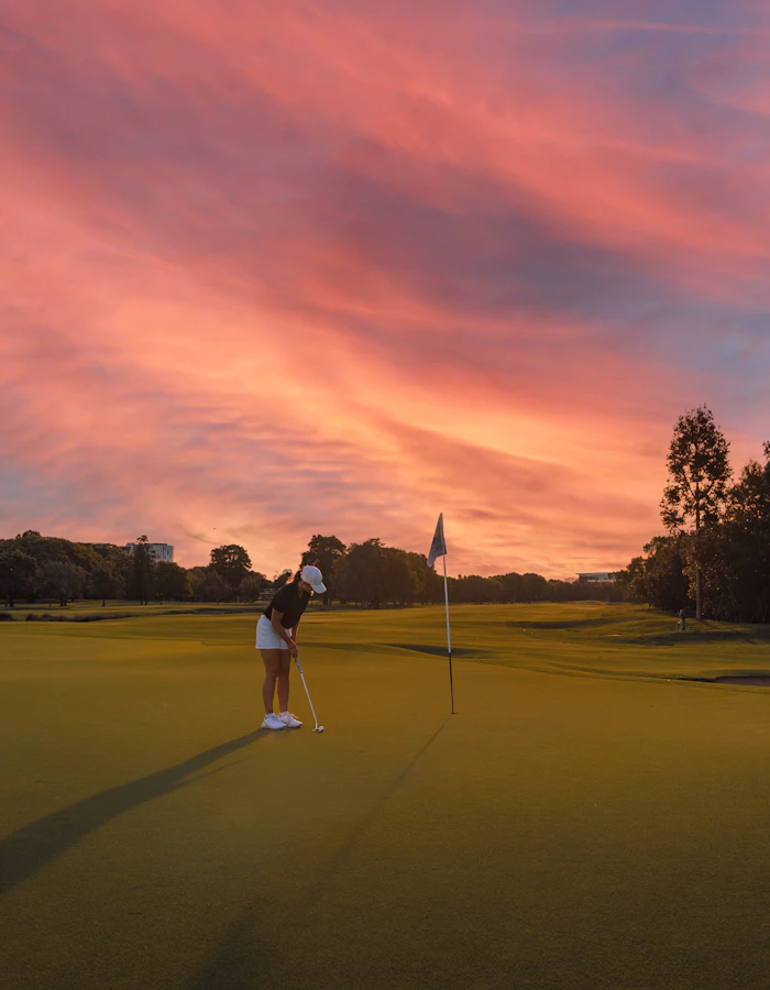 A golfer on the green under a pink evening sky